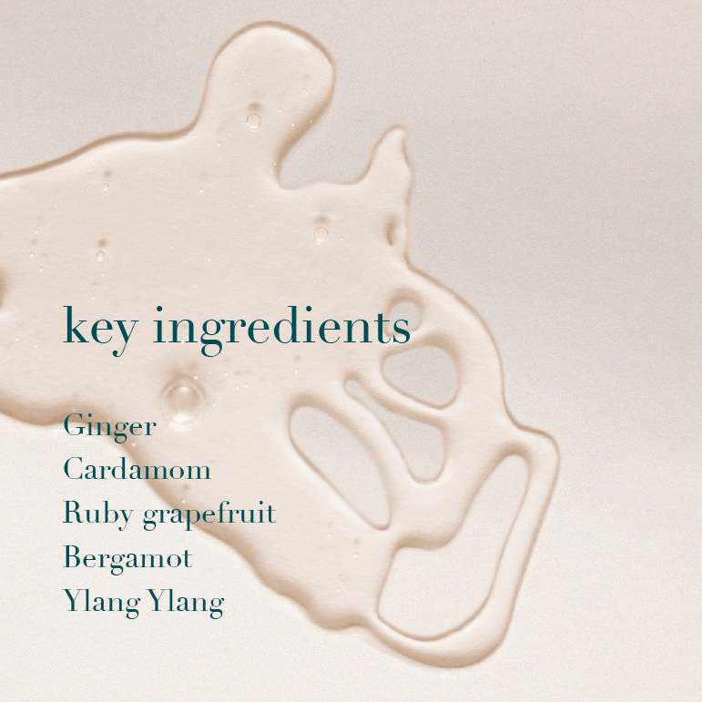 A close-up of a glossy beige liquid splash on a light warm background, with the text 'key ingredients' and a list reading Ginger, Cardamom, Ruby grapefruit, Bergamot, and Ylang Ylang in dark teal.